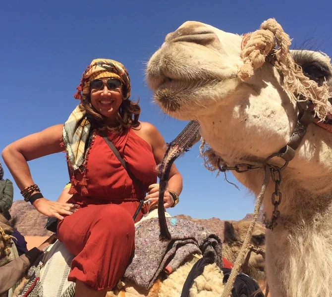 Lisa next to a camel in a red desert